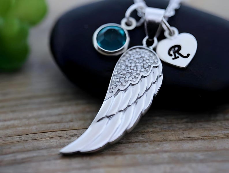 May include: Silver angel wing pendant necklace with a turquoise blue gemstone and a silver heart charm with the letter R.