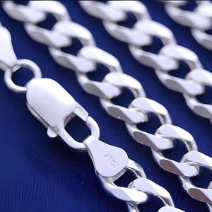May include: Silver curb chain necklace with a lobster clasp. The chain is made of multiple links that are interlocked to form a strong and durable chain.