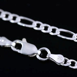 May include: A shiny silver figaro chain necklace featuring a polished finish and a secure lobster claw clasp. The metal links are arranged in a repeating pattern of three small circular links followed by one elongated oval link.