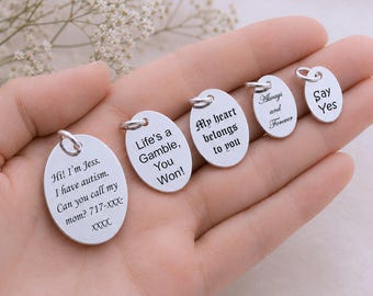 May include: Five silver-toned oval charms with jump rings, each featuring black engraved text. The inscriptions read: Hi! I'm Jess. I have autism. Can you call my mom? 717-XXX-XXXX, Life's a Gamble, You Won!, My heart belongs to you, Always and Forever, and Say Yes.