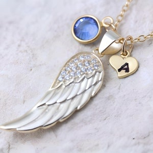 May include: Gold necklace with a small blue gemstone, a heart charm with the letter 'A' engraved on it, and a large angel wing pendant with clear rhinestones.