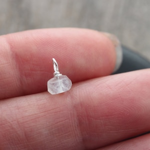 May include: A small, clear, faceted crystal charm with a silver wire loop. The charm is about the size of a 10 pence coin.
