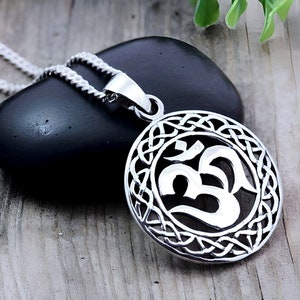 May include: Silver pendant necklace featuring an Om symbol surrounded by a Celtic knot design. The pendant is round and hangs from a silver chain.