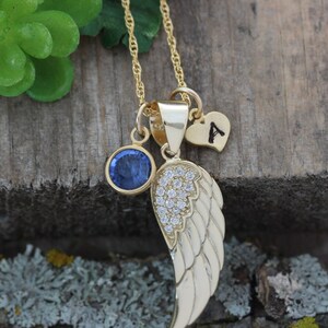 May include: Gold necklace with a blue gemstone, a small heart charm with the letter 'A' and a gold wing charm with clear crystals.