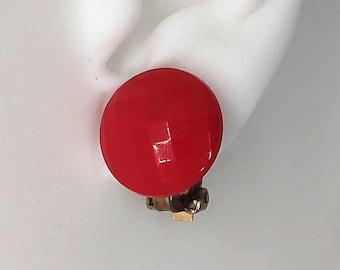May include: Red clip-on earrings with a shiny finish. The earrings are on a white background.