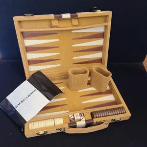 May include: Open backgammon set with a corduroy-like texture in tan and brown. The set includes dice, game pieces, and dice cups. The game board is open, revealing the playing surface with brown and white triangles. The instruction booklet reads "BACKGAMMON".