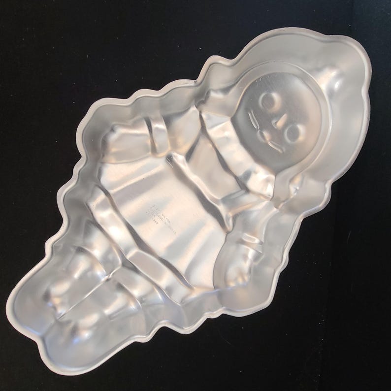 Puede incluir: Molde para pastel de metal plateado con forma de mu&ntilde;eco de nieve. El molde tiene detalles como una cara con ojos, nariz y boca. El cuerpo del mu&ntilde;eco de nieve tambi&eacute;n est&aacute; detallado con brazos y una forma redondeada.