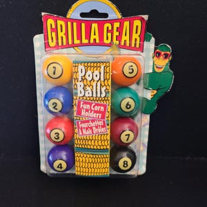 May include: A package of eight colorful pool ball-shaped corn holders. The package reads "GRILLA GEAR Pool Balls Fun Corn Holders". Each holder is numbered 1-8 and is a different color, including yellow, blue, red, purple, orange, green, maroon, and black.