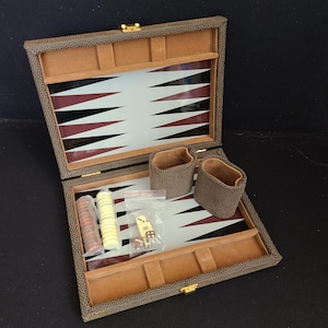 May include: Open backgammon set with a brown textured exterior and a tan interior. The game board features a white surface with black and burgundy triangles. Includes dice, game pieces, and dice cups.