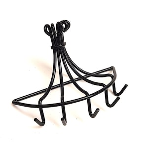 May include: A black metal soap dish with a curved design and six hooks. The dish has a decorative top with looped details. The hooks are evenly spaced along the bottom edge, perfect for holding soap.