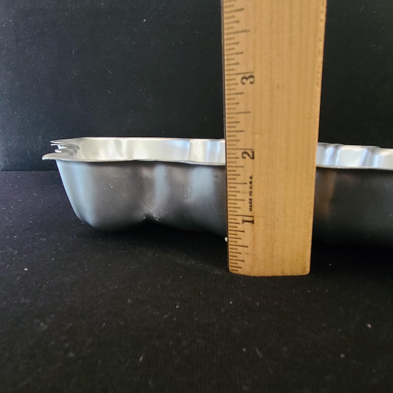 Puede incluir: Una bandeja para hornear plateada con bordes festoneados y una regla de madera al lado. La bandeja tiene aproximadamente 5 cm de profundidad. La regla muestra medidas en pulgadas.