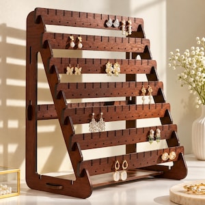May include: A dark brown wooden earring display stand featuring six tiered horizontal bars with pre-cut slots and holes for organizing jewelry. The structure is supported by two side panels and holds various pairs of earrings, including studs and dangles.