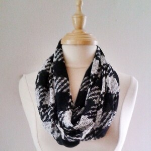 May include: A black and white infinity scarf with a plaid pattern. The scarf is displayed on a white mannequin.
