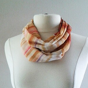 Peut inclure: Une écharpe infinie rayée dans les tons orange, rose et blanc. L'écharpe est faite d'un tissu doux et léger, parfait pour superposer en automne ou en hiver.