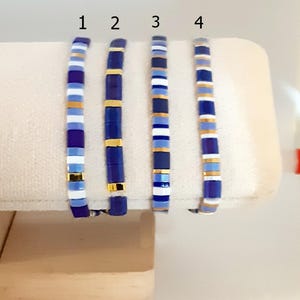 Peut inclure: Quatre bracelets en perles bleues et dorées avec des accents blancs. Les bracelets sont numérotés de 1 à 4.