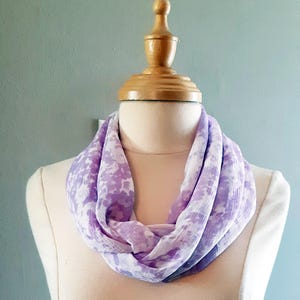 Peut inclure: Une écharpe infinie à motif violet et blanc en tissu doux et transparent.