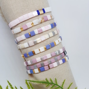 May include: A stack of colourful bracelets with white, pink and blue tiles. The bracelets are made of ceramic and have a glossy finish.