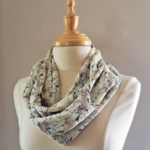 May include: A cream-colored infinity scarf with a floral print in black and pink.