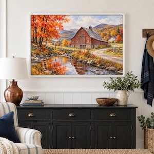 May include: A framed landscape painting depicting a red barn situated beside a flowing stream, surrounded by vibrant autumn foliage in shades of orange and yellow, with rolling mountains visible in the distant background under a cloudy sky.