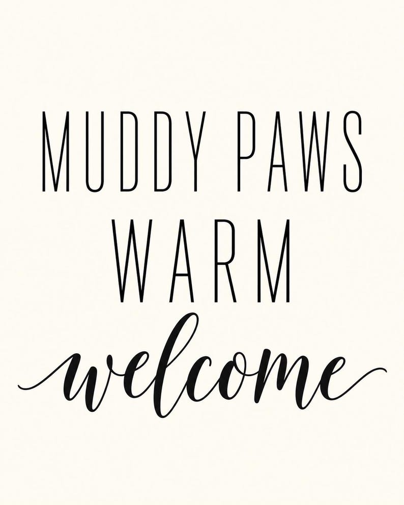 May include: A rectangular sign featuring the black text MUDDY PAWS WARM welcome printed on a solid off-white background. The words MUDDY PAWS and WARM are in a tall, thin, sans-serif font, while the word welcome is in a cursive script.