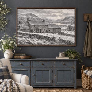 May include: A framed black and white landscape print depicting a stone farmhouse with a slate roof, a stone wall, and a wooden gate in a mountainous valley. The scene includes a lake in the distance under a cloudy sky, presented in a brown frame.
