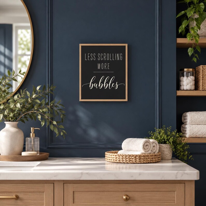 May include: A rectangular wall sign with a light wood frame and a black background. The text in white reads LESS SCROLLING MORE bubbles, with the word bubbles written in a cursive script font. The sign is mounted on a dark blue wall.
