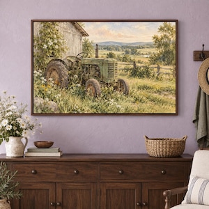 May include: A framed landscape painting depicting a weathered green tractor parked beside a rustic wooden barn in a grassy field filled with wildflowers, with rolling hills and a soft sky visible in the background of the rural scene.