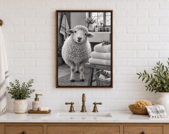 May include: A framed black and white wall art print featuring a fluffy sheep standing in a bathroom setting. The image shows the sheep positioned near a wooden stool stacked with folded towels, a woven basket, and a sink area.