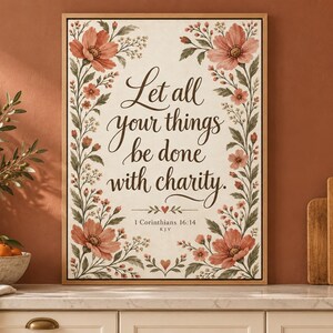 May include: A rectangular wall art print in a light wood frame featuring the text Let all your things be done with charity and 1 Corinthians 16:14 KJV. The design is bordered by watercolor-style pink flowers and green foliage.