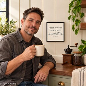 May include: A square wall sign with a black frame and white background features the black text FRESH COFFEE UNHURRIED conversation. The sign is displayed on a white panelled wall next to a coffee grinder and a jar of coffee beans.