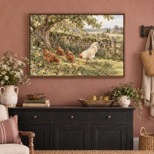 May include: A rectangular framed wall art print depicting a rural landscape with a stone wall, a large tree, and three chickens, including one white rooster and two brown hens, foraging on the ground in a grassy field.