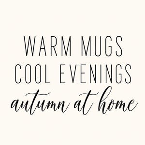 May include: A white rectangular sign featuring black text. The top two lines read WARM MUGS and COOL EVENINGS in a clean, sans-serif font. The bottom line features the phrase autumn at home written in a flowing, cursive script font.