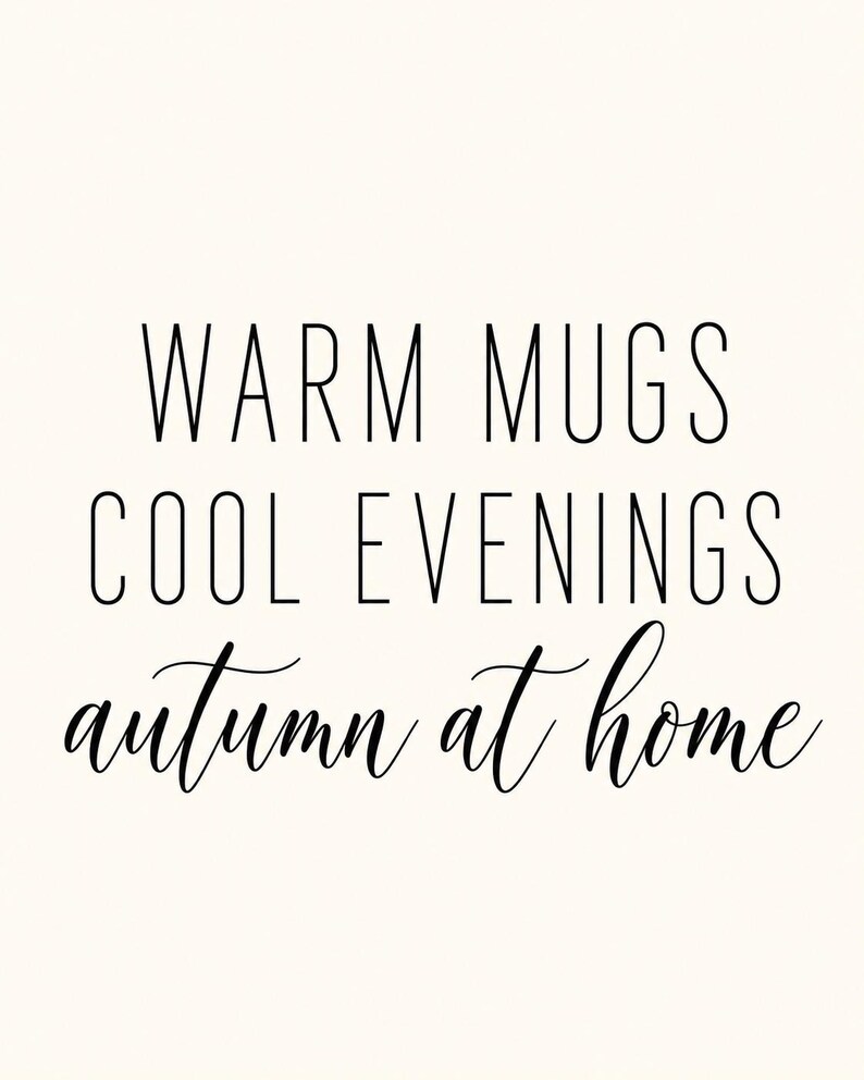 May include: A white rectangular sign featuring black text. The top two lines read WARM MUGS and COOL EVENINGS in a clean, sans-serif font. The bottom line features the phrase autumn at home written in a flowing, cursive script font.