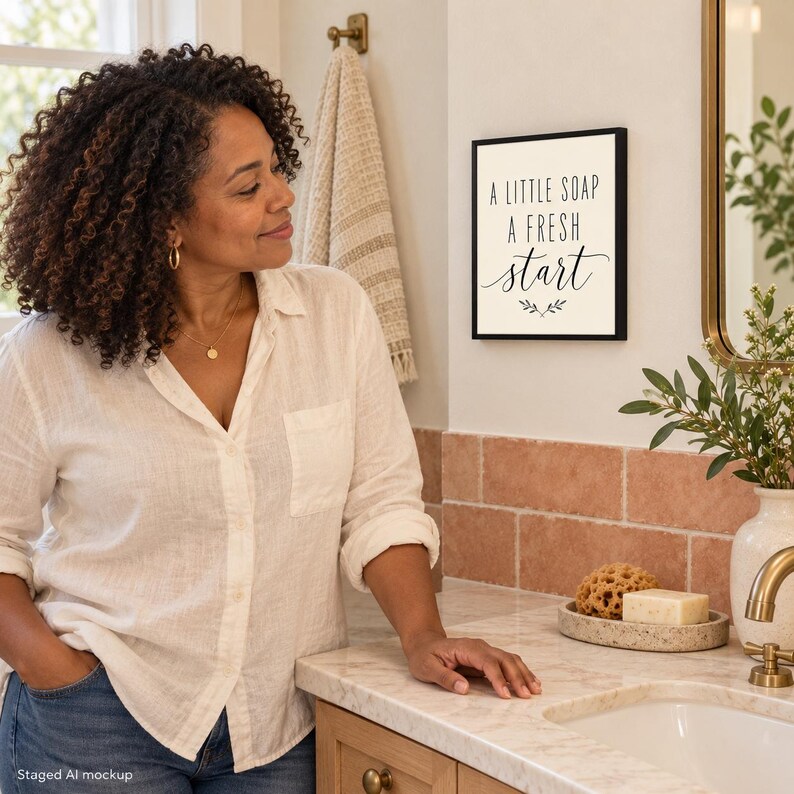 May include: A square wall sign with a black frame and a white background featuring the black text A LITTLE SOAP A FRESH start with a small decorative leaf graphic centered below the text, mounted on a bathroom wall.