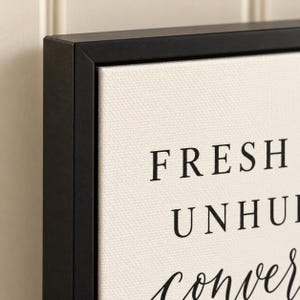 May include: A framed canvas wall art piece featuring a black matte frame and a cream-coloured textured canvas. The text printed in black ink reads FRESH, UNHURRIED, and the word conversation in a cursive script font is partially visible at the bottom.