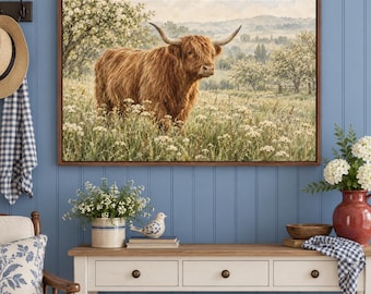 May include: A rectangular wall art print featuring a long-haired Highland cow standing in a field of white wildflowers. The scene includes rolling hills and trees in the background, all enclosed within a simple brown wooden frame.