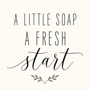 May include: A white rectangular sign featuring the black text A LITTLE SOAP A FRESH START in a combination of sans-serif and cursive fonts. Below the text is a small, simple black line drawing of two symmetrical leafy branches.