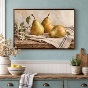 May include: A framed rectangular wall art print depicting three ripe green and yellow pears resting on a textured beige linen cloth atop a weathered wooden surface, accompanied by a small sprig of white pear blossoms with green leaves.
