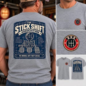 May include: A heather gray t-shirt featuring a blue blueprint graphic on the back with a manual gear shifter, three pedals, and text reading THE STICK SHIFT ASSOCIATION, 3 PEDALS, 5 GEARS, and THE ORIGINAL ANTI-THEFT DEVICE. A small circular logo is on the front.