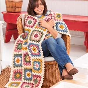 Peut inclure: Une couverture en crochet faite à la main avec un motif de carrés granny colorés. La couverture est composée de carrés individuels dans des tons de rose, bleu, jaune, vert et crème, assemblés par une bordure couleur crème.