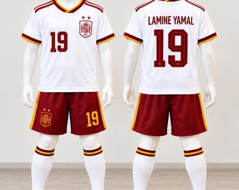 Peut inclure: Un ensemble de football blanc et bordeaux comprenant un maillot et un short avec le numéro 19, l'écusson de l'équipe nationale espagnole et le nom Lamine Yamal au dos. La tenue inclut des chaussettes blanches à rayures bordeaux et jaunes.