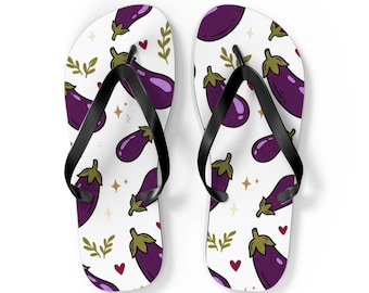 May include: A pair of white flip-flops featuring a repeating pattern of purple eggplants, small green leafy sprigs, tiny red hearts, and gold four-pointed stars. The footwear includes black rubber straps attached to the white soles.