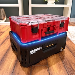 May include: A red and black modular tool storage system featuring a red top organizer with a clear lid and black latches, stacked on a black base unit labeled Toughbuilt Stacktech with a glowing blue light accent along the top edge.