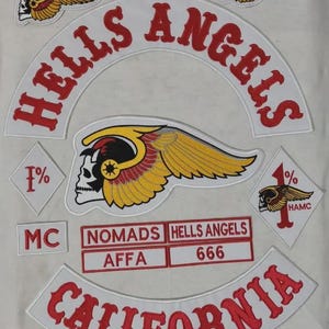May include: A collection of embroidered patches featuring the text HELLS ANGELS and CALIFORNIA in red on white backgrounds. Includes a central winged skull emblem, two diamond-shaped 1% patches, and rectangular labels reading NOMADS, AFFA, and 666.
