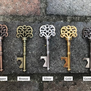 May include: Five ornate key-shaped bottle openers in different finishes: copper, bronze, silver, gold, and gunmetal. Each opener features a decorative, intricate design.
