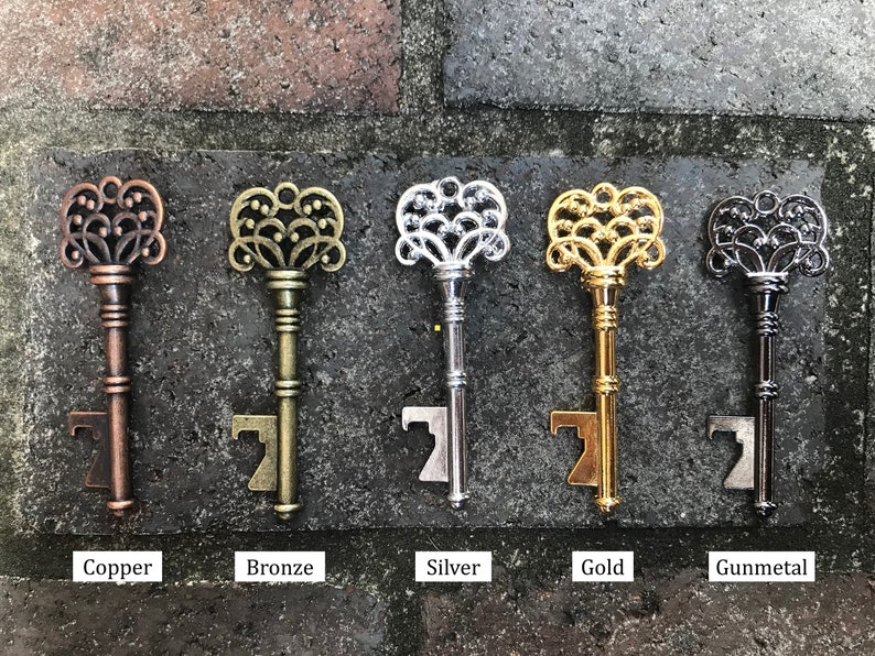 May include: Five ornate key-shaped bottle openers in different finishes: copper, bronze, silver, gold, and gunmetal. Each opener features a decorative, intricate design.