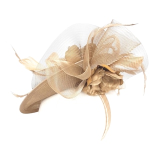 Op de afbeelding: Een beige fascinator met een mesh sluier, veren en een stoffen bloem. De hoofdbedekking is ontworpen met gelaagde stof en decoratieve elementen, geschikt voor formele evenementen.