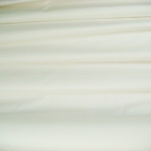 May include: A smooth, white fabric with soft folds and wrinkles. The fabric is a light cream color and has a subtle sheen.