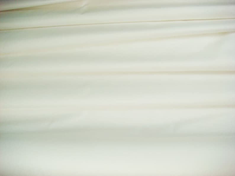 May include: A smooth, white fabric with soft folds and wrinkles. The fabric is a light cream color and has a subtle sheen.