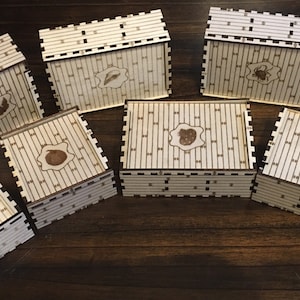 May include: Seven wooden boxes with different animal illustrations on the top. The boxes are made of light brown wood and have a light brown background with a pattern of vertical lines. The boxes are arranged in a semi-circle on a wooden surface.
